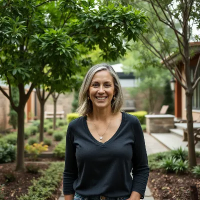 Elena Whitmore, arborist and landscape designer, smiling confidently amidst a lush, well-designed garden space.